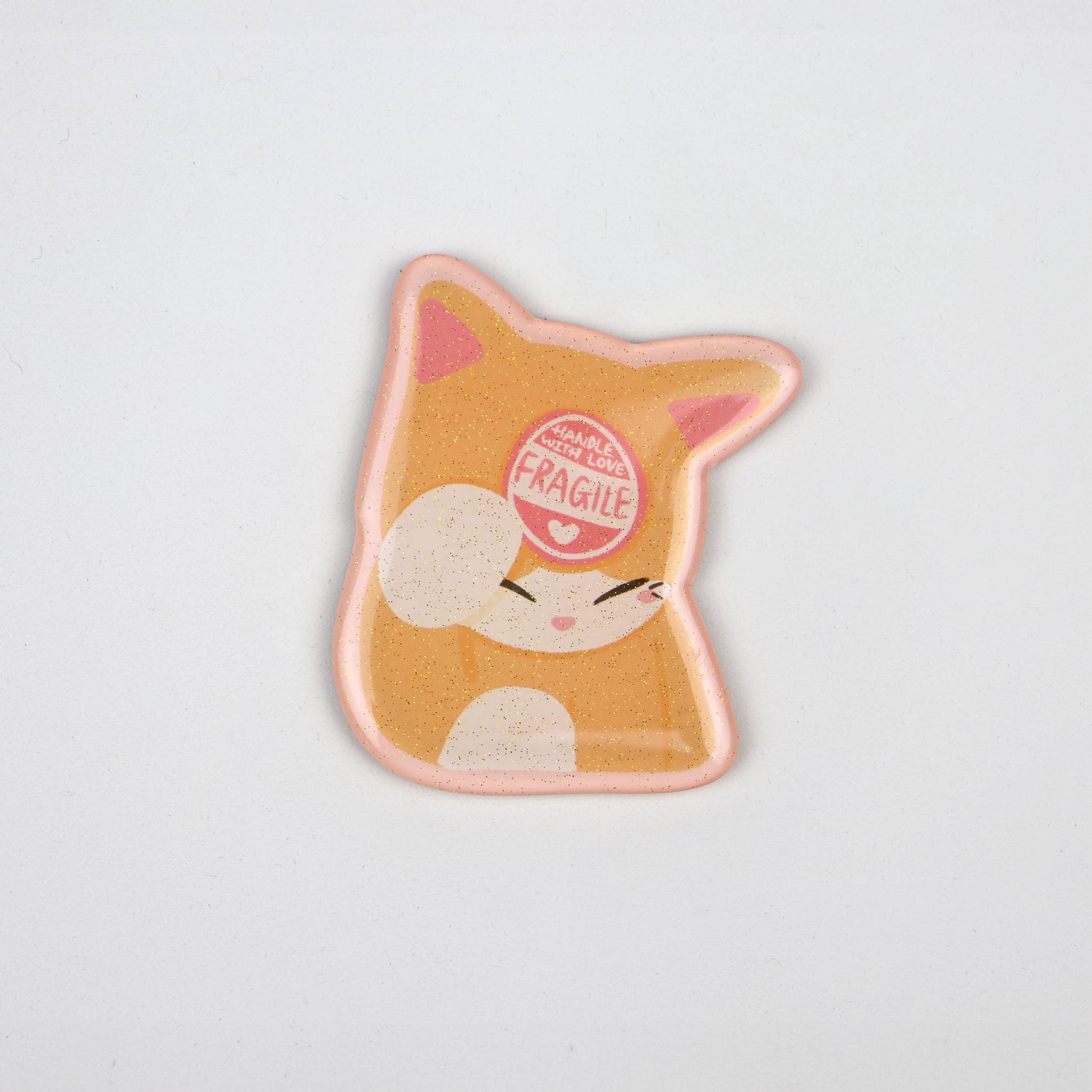 An acrylic magnet in the shape of a cat with a 'Fragile' sticker on its head.