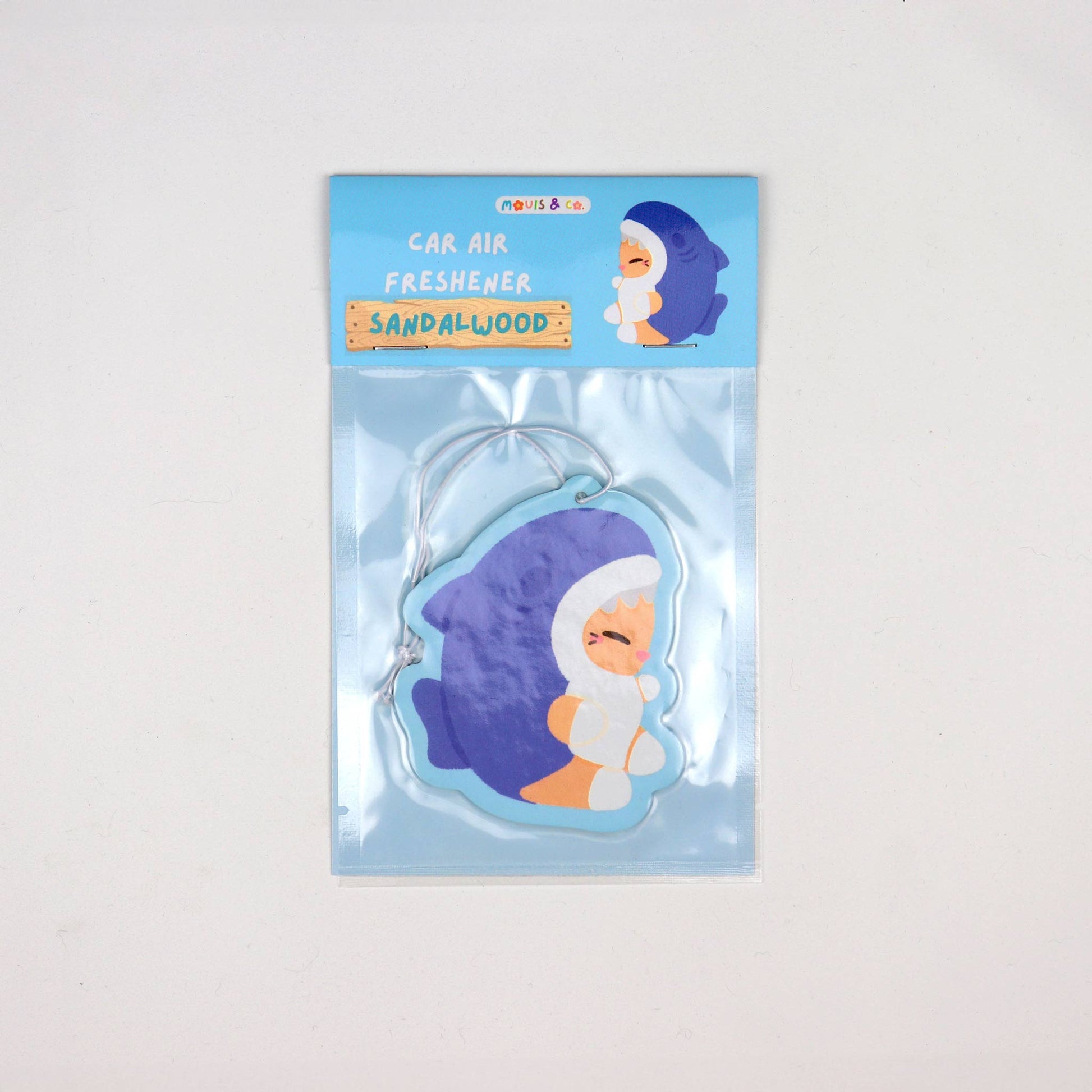 Sandalwood-scented car air freshener featuring a cute cat in a blue shark costume, illustrated by Melbourne artist duo Mouis Land. Packaged in a clear pouch with blue header card.