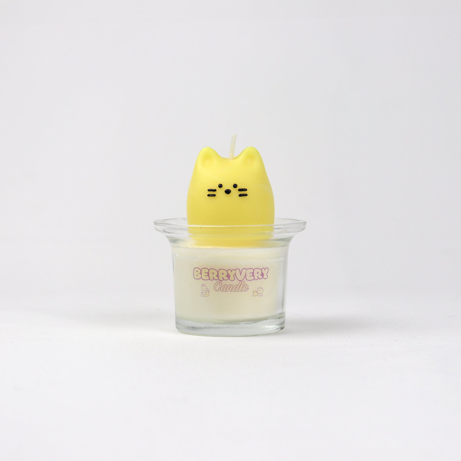 Yellow soy wax candle shaped like a cat face sitting in a glass cup with “BERRYVERYCANDLE” label.