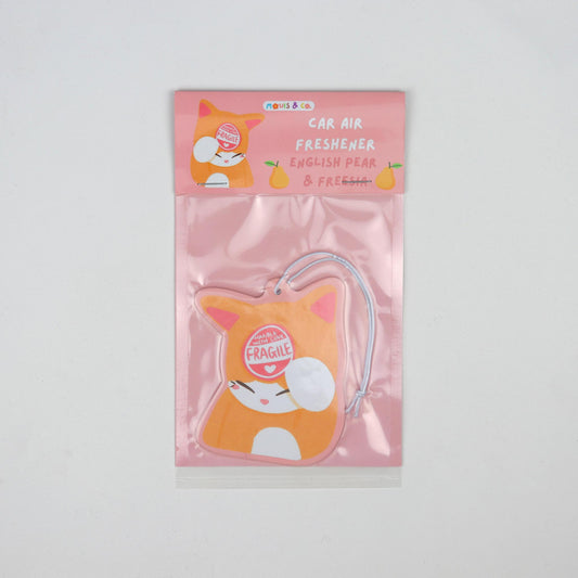 English pear and freesia-scented car air freshener featuring an orange cat with a “Handle with Care – I'm Fragile” sticker, designed by Melbourne artists Mouis Land. Packaged in a pink pouch.