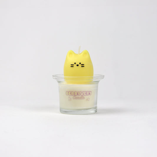 Yellow soy wax candle shaped like a cat face sitting in a glass cup with “BERRYVERYCANDLE” label.